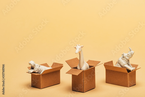 Photography White toy hippopotamus, rhinoceros and giraffe in cardboard boxes on yellow back