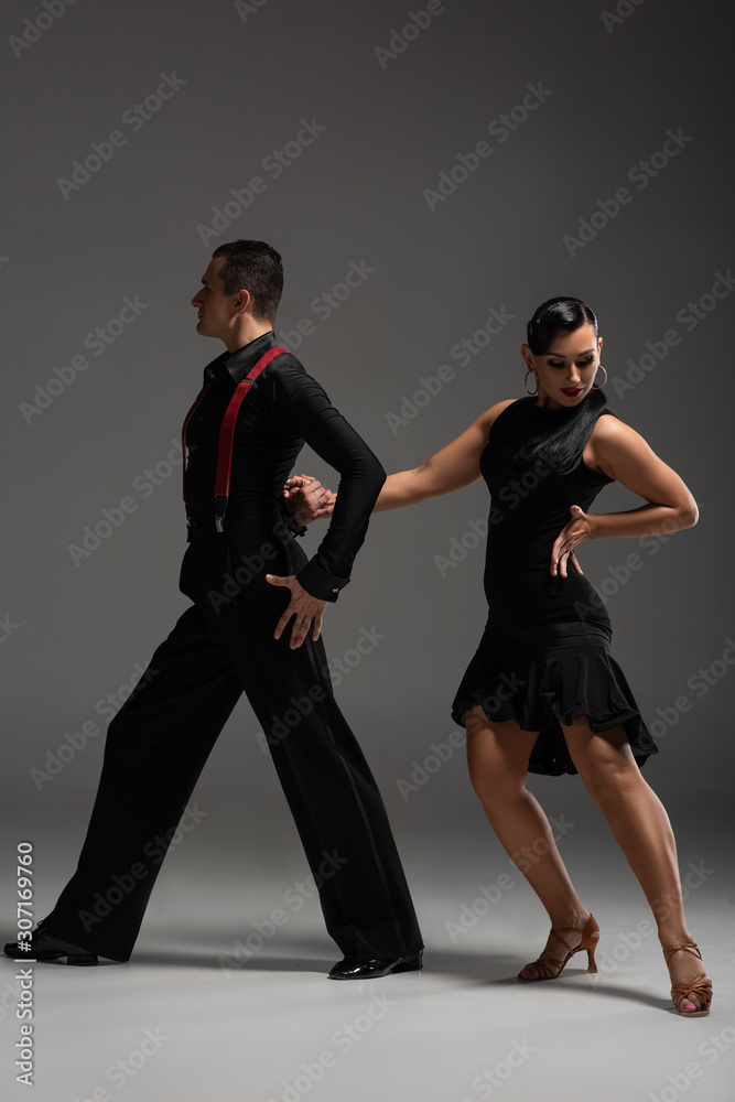 stylish couple of dancers in black clothing performing tango on grey background