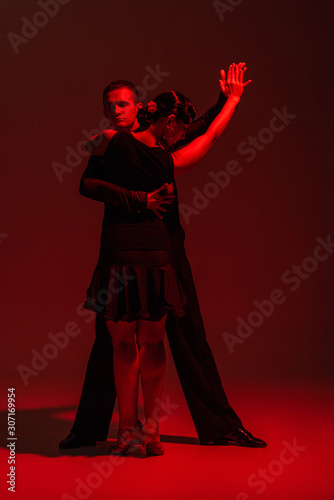 elegant couple of dancers in black clothing performing tango on dark background with red lighting