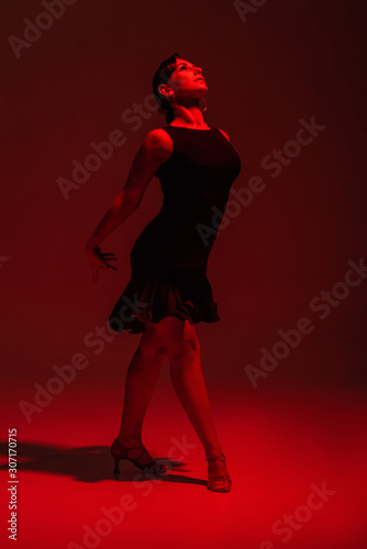 beautiful dancer in black dress performing tango on dark background with red lighting