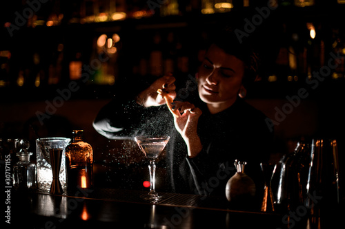 Bartender girl sprinkling on a alcoholic drink in the cocktail glass with a orange zest juice