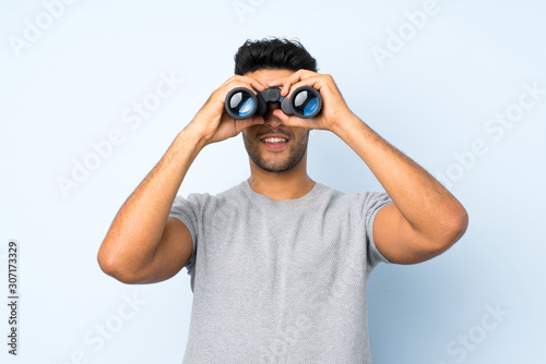 Young handsome man over isolated background with black binoculars