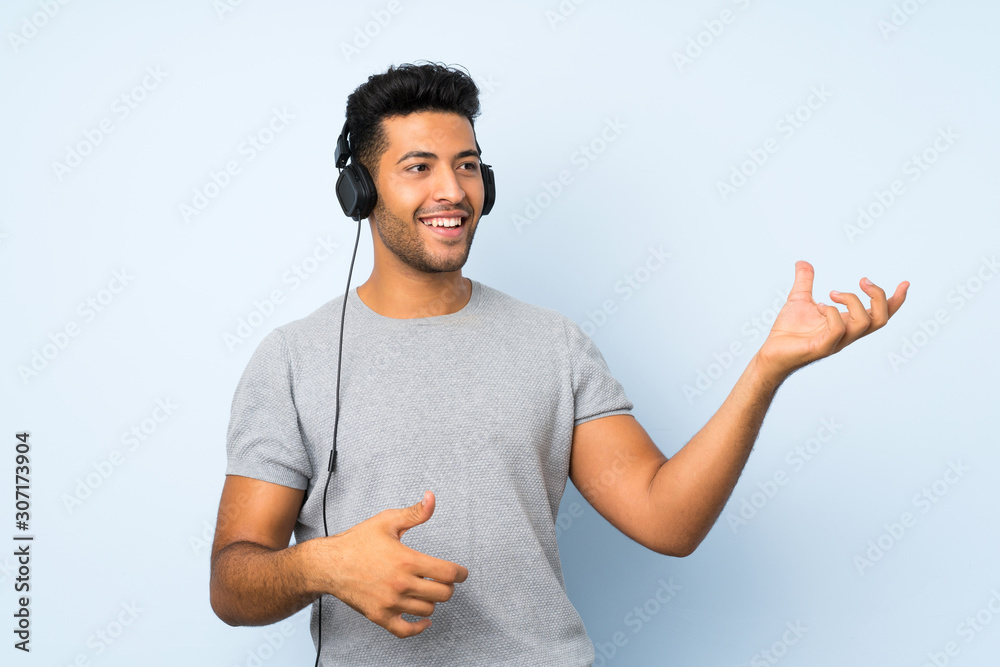 Young handsome man over isolated background using the mobile with headphones and dancing