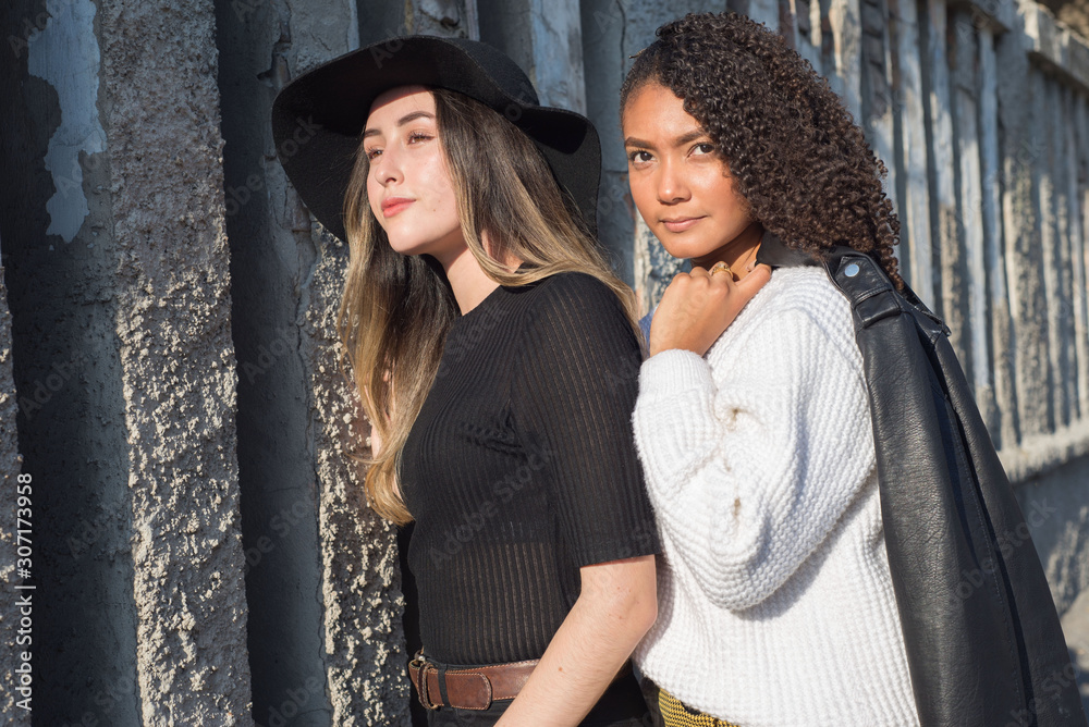 Portrait of a pair of beautiful fashionable Spanish girls standing against a texture wall. Fashion photography Street art Portrait of a pair of beautiful fashionable Spanish girls standing against a texture wall. Fashion photography Street art