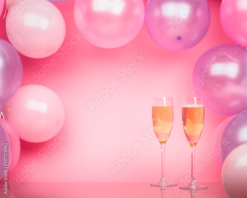 Two glasses of champagne on a pink background with pink and purple balloons. Bright background for celebration.