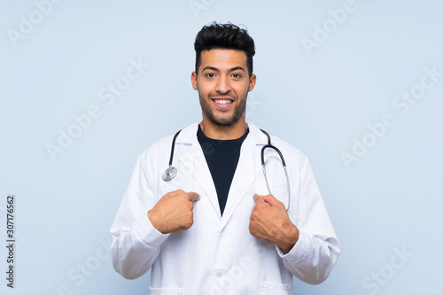 Young doctor man over isolated blue wall with surprise facial expression