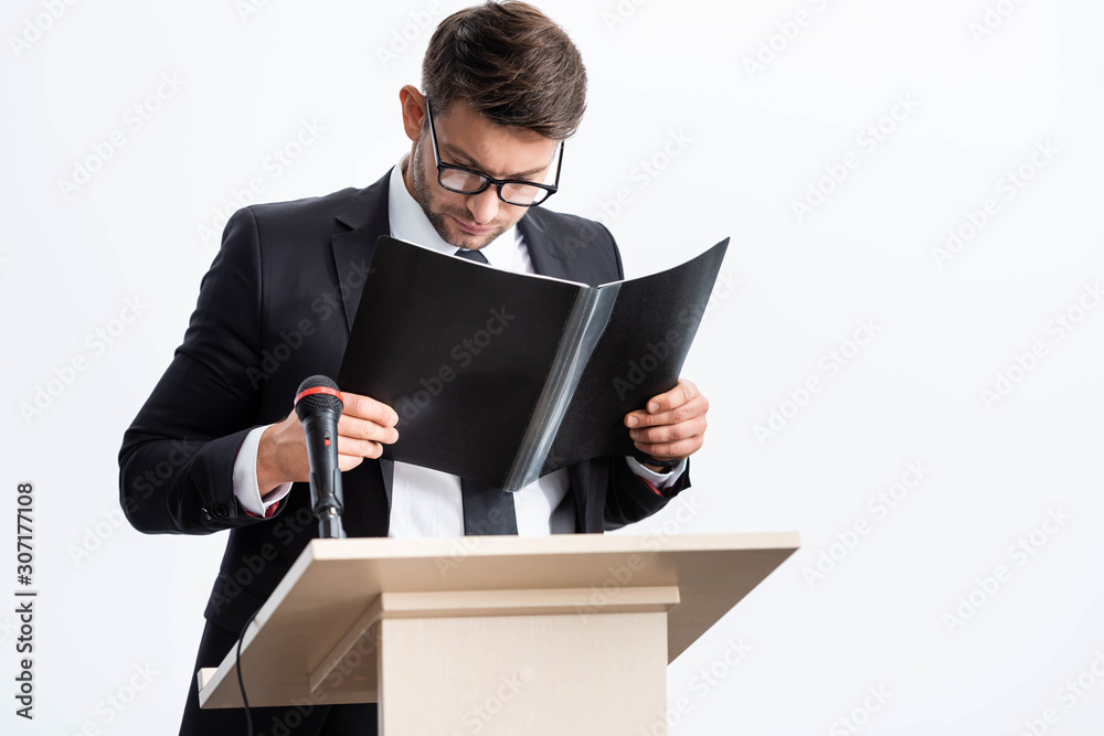 businessman in suit standing at podium tribune and holding folder during conference isolated on white businessman in suit standing at podium tribune and holding folder during conference isolated on white