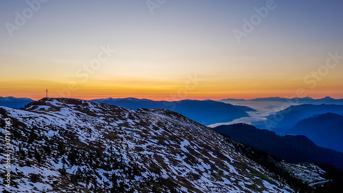 Sunrise over a fog covered snowy Alps in Goldeck, Austria. The sky line is bursting with orange and yellow. There is thick fog in the valley. Soft sunrise colours. Endless mountain chains in the back photo