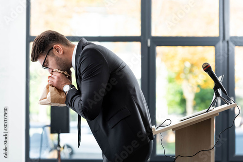 side view of scared businessman in suit breathing in paper bag during conference photo