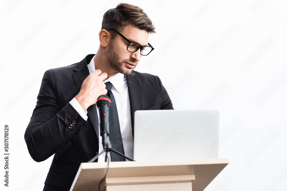 stressed businessman in suit standing at podium tribune and looking at laptop during conference isolated on white stressed businessman in suit standing at podium tribune and looking at laptop during conference isolated on white