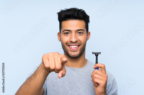 Young man shaving his beard over isolated blue background points finger at you with a confident expression