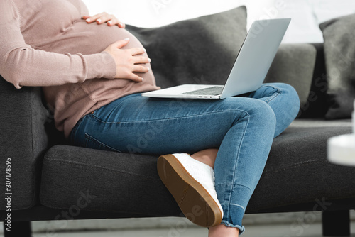 cropped view of pregnant woman touching belly and having online consultation with doctor on laptop at home