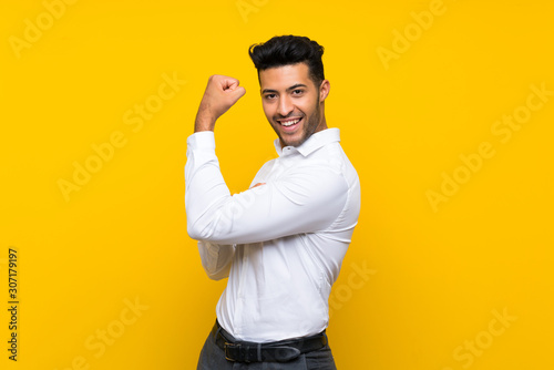 Foto Young handsome man over isolated yellow background making strong gesture