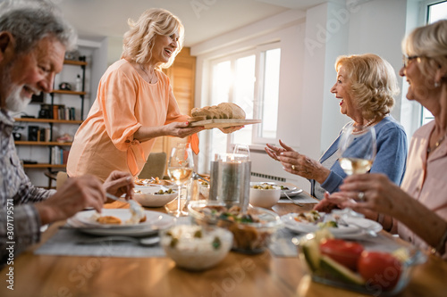 Happy senior woman serving bread to her friends during lunch time at home.
