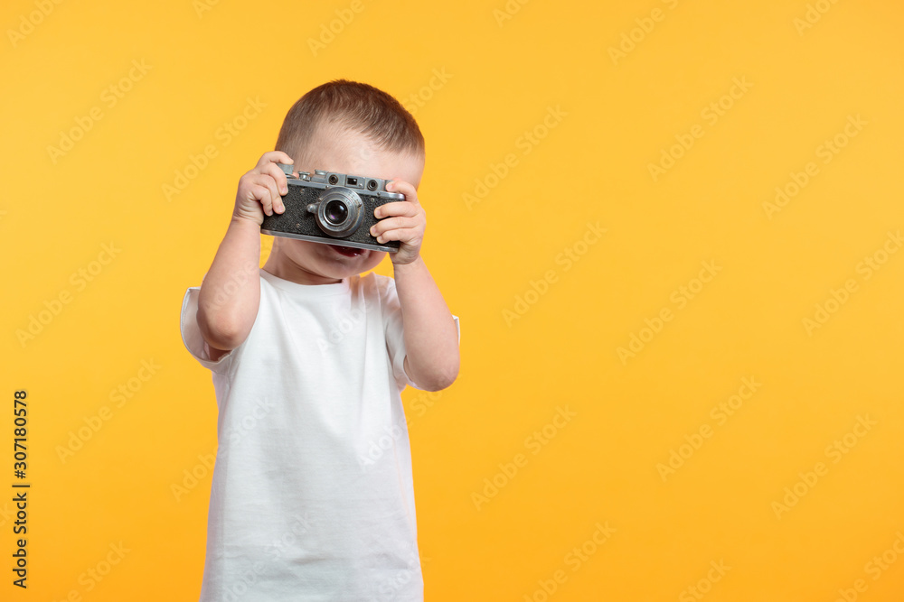 Boy taking a picture with a retro camera over yellow background