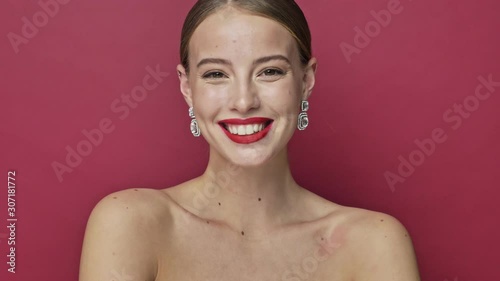 Positive young woman with red lipstick and earrings is waving her hand isolated over red background photo