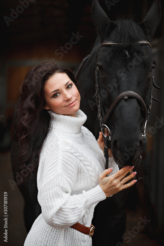 Beautiful brunette girl in white cloth with her black horse