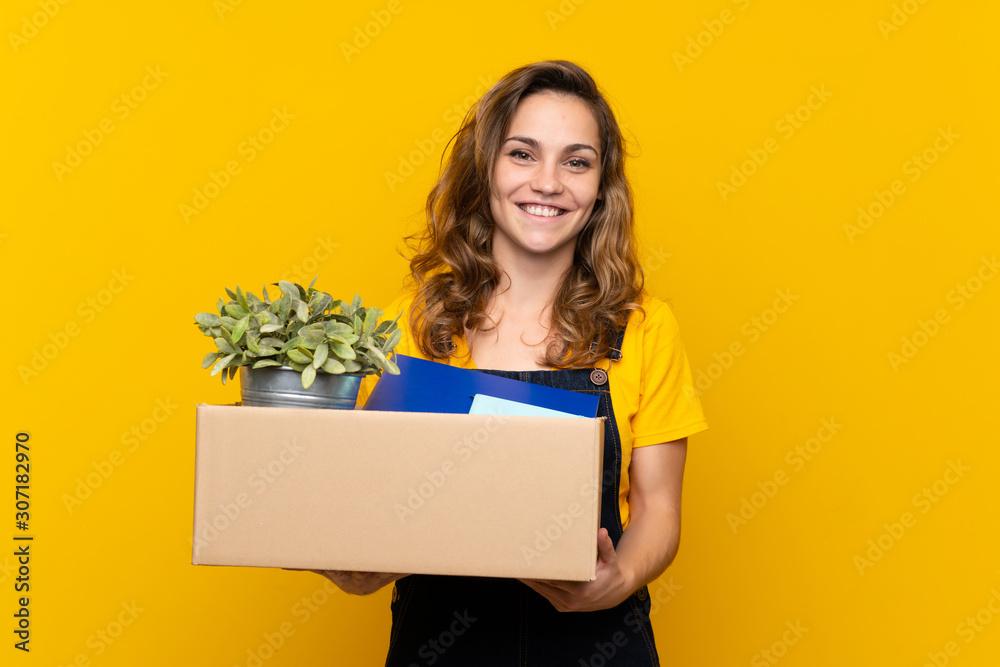 Young blonde girl making a move while picking up a box full of things smiling a lot Young blonde girl making a move while picking up a box full of things smiling a lot