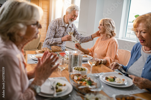 Happy senior couple toasting with wine while enjoying in lunch with friends at home.