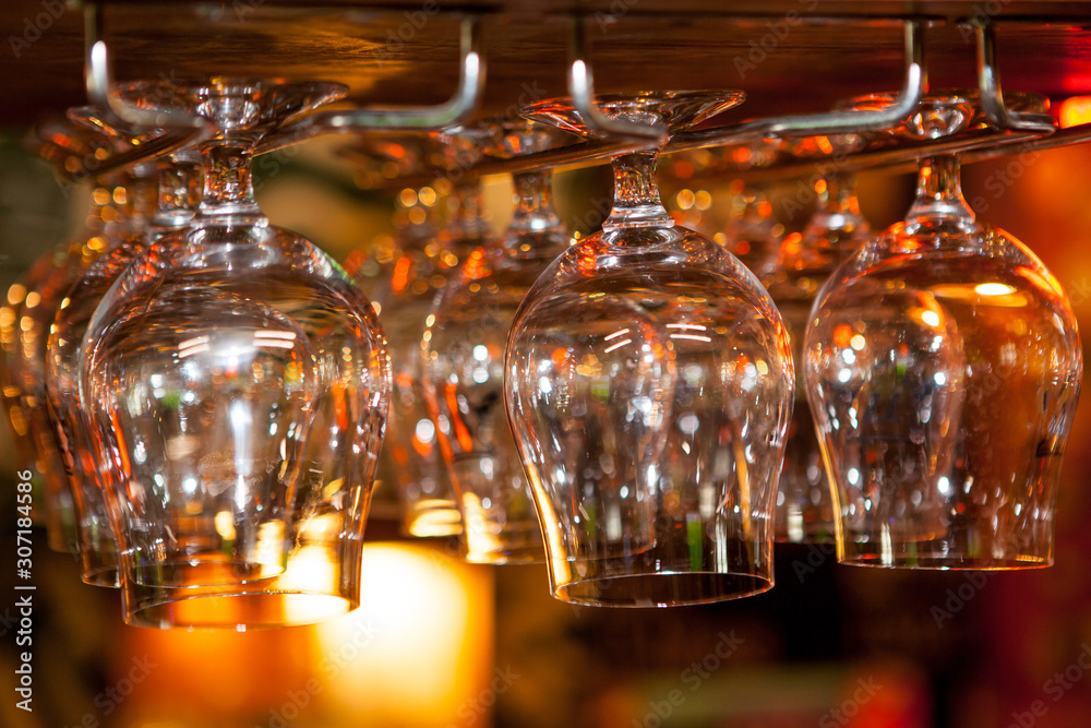 Wine and beer glasses on lit bar, lined up neatly. On the shelf of a resturant/bar at night with glowing glass