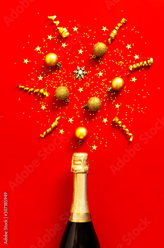 Christmas and New Year background. Champagne bottle, golden christmas balls, festive ribbons, fir branches, star confetti on red background top view. Flat lay holiday card. Festive decorations 2020