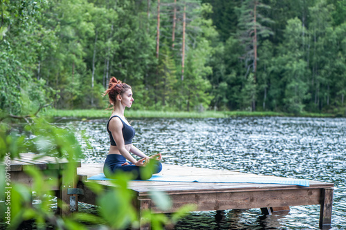 Young girl practicing yoga in the nature on the lake. Female happiness. Landscape background