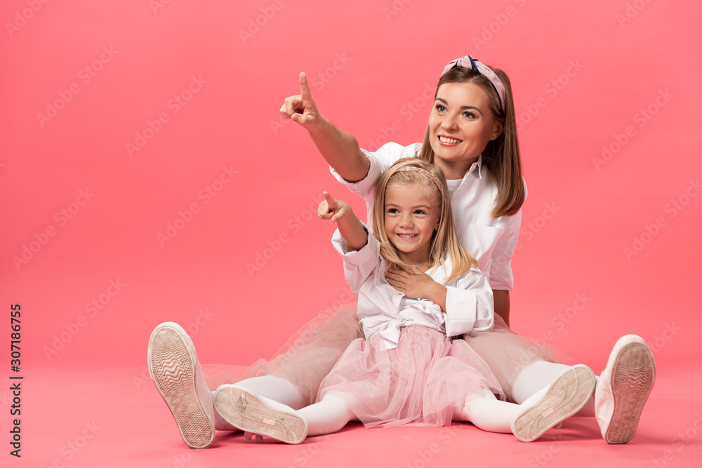 smiling daughter and mother pointing with fingers on pink background - obrazy, fototapety, plakaty 