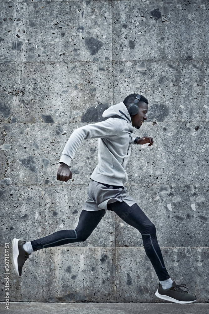 Athletic man is running near the grey wall
