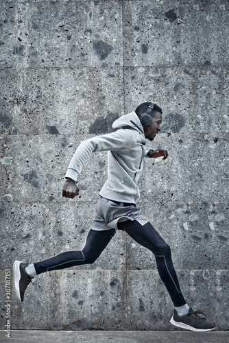 Athletic man is running near the grey wall © Alex