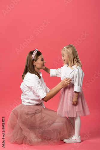 side view of smiling daughter and mother hugging on pink background