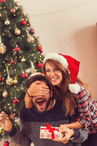 Girlfriend holding boyfriends eyes and giving his Christmas gift