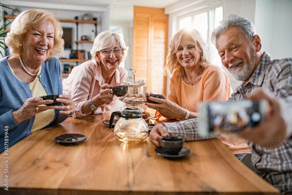 Group of happy seniors taking selfie while drinking tea at home.