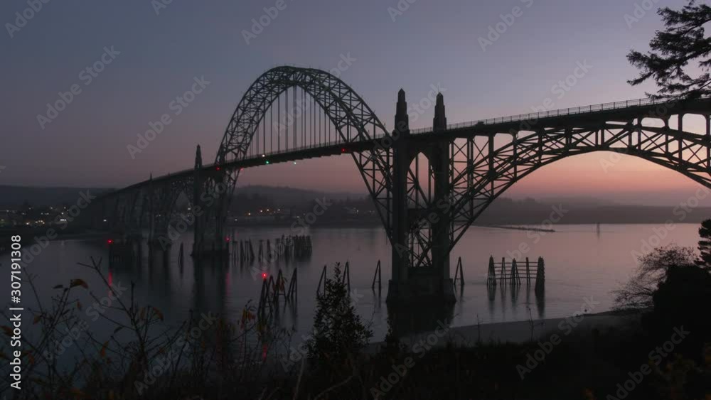 Beautiful shot of the Yaquina Bay Bridge in Newport, Oregon at sunset silhouetted in the purple darkening sky while lights of cars cross on Highway 101 Beautiful shot of the Yaquina Bay Bridge in Newport, Oregon at sunset silhouetted in the purple darkening sky while lights of cars cross on Highway 101
