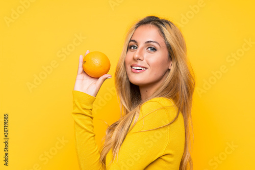 Young blonde woman holding an orange over yellow background