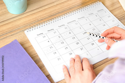 Woman with calendar at wooden table in office, closeup