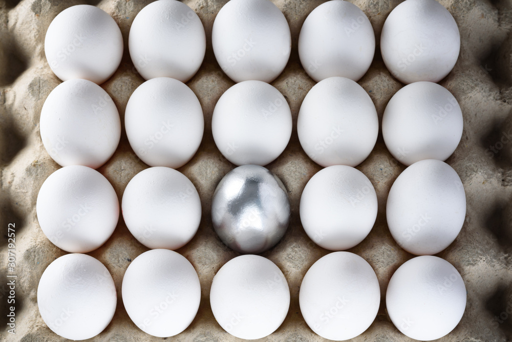 Silver egg standing out from crowd of plenty identical white eggs in carton box background. Leadership, uniqueness, independence, new idea, initiative, strategy, dissent, think different concept. Silver egg standing out from crowd of plenty identical white eggs in carton box background. Leadership, uniqueness, independence, new idea, initiative, strategy, dissent, think different concept.