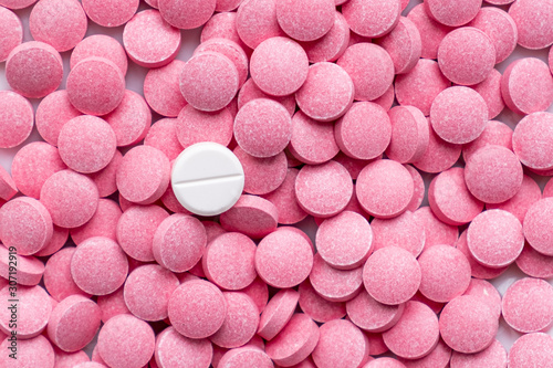 Pile of pink pills and around a white one. Medication, self-treatment or placebo concept: one tablet is different from the lot of others photo