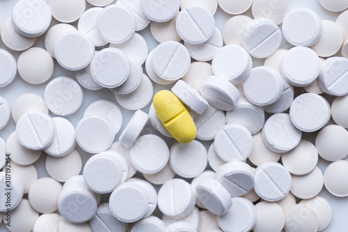 Pile of white pills and around a yellow one. The concept of different, alternative or placebo treatment photo