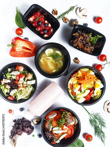 Culinary dishes made from natural products in a plastic bowl on the background with ingredients for cooking. Healthy food delivery concept. Top view.