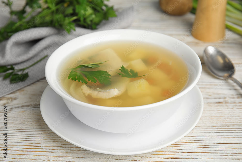 Delicious fish soup in bowl on white wooden table Delicious fish soup in bowl on white wooden table