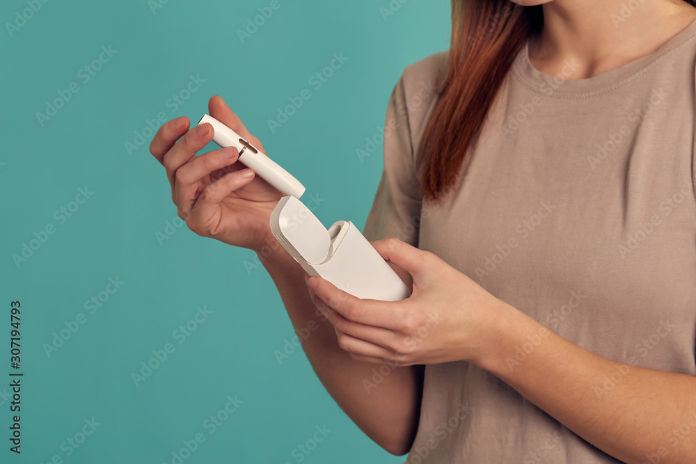 Obraz premium Electronic Cigarette Technology. Tobacco IQOS system. Close-up of a girl smoking an electric hybrid cigarette with a heating pad. tobacco heating system.