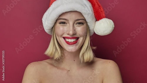 Nice attractive young woman with red lipstick wearing santa clause hat is sending an air kiss isolated over red background
