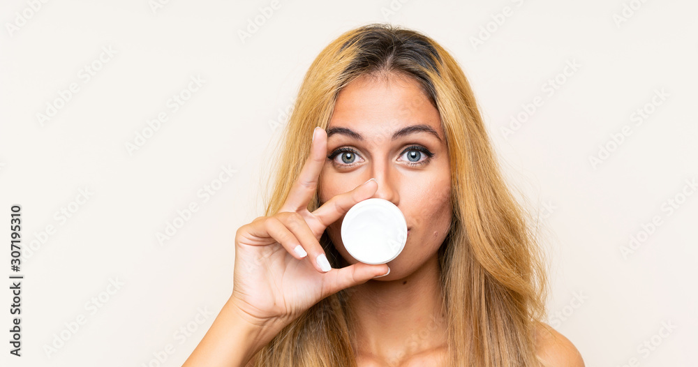 Young blonde woman with moisturizer over isolated background Young blonde woman with moisturizer over isolated background