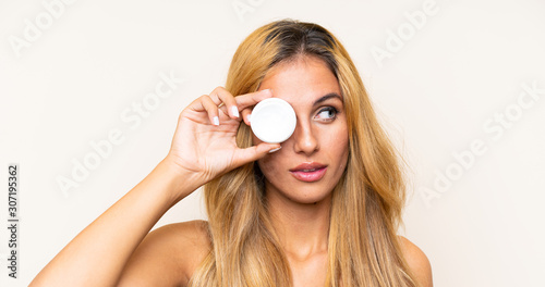 Young blonde woman with moisturizer over isolated background