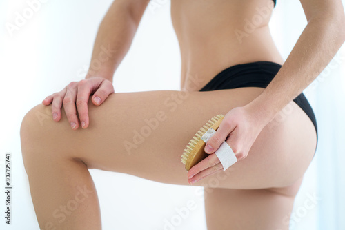 Woman brushing skin buttocks and butt with a dry wooden brush to prevent and treatment cellulite and body problem after shower at home. Skin health