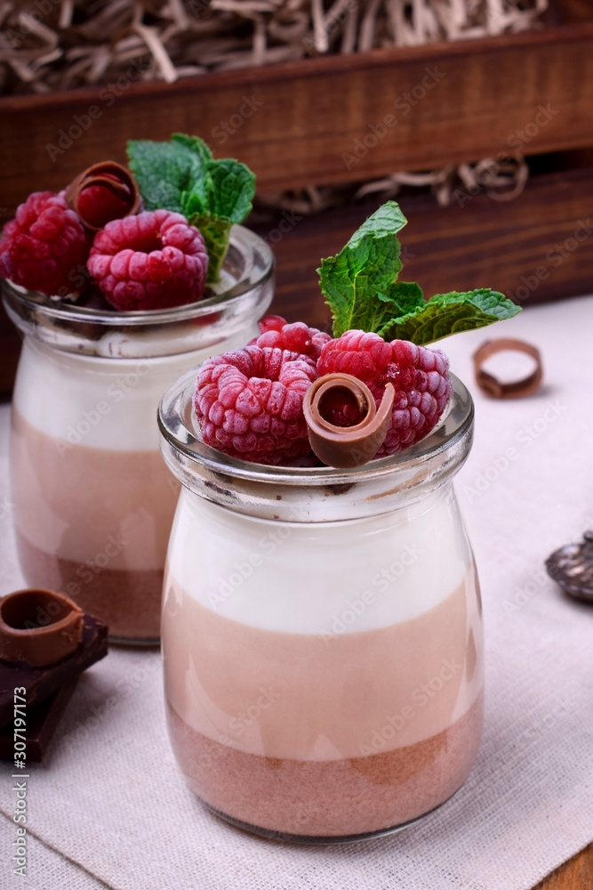 Three chocolate mousse dessert in a glass jar topped with frozen raspberries and mint Three chocolate mousse dessert in a glass jar topped with frozen raspberries and mint