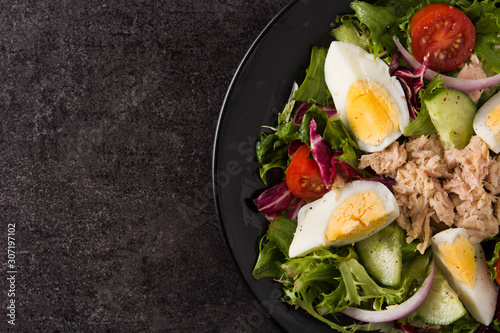 Salad with tuna, egg and vegetables on black background top view copy space	