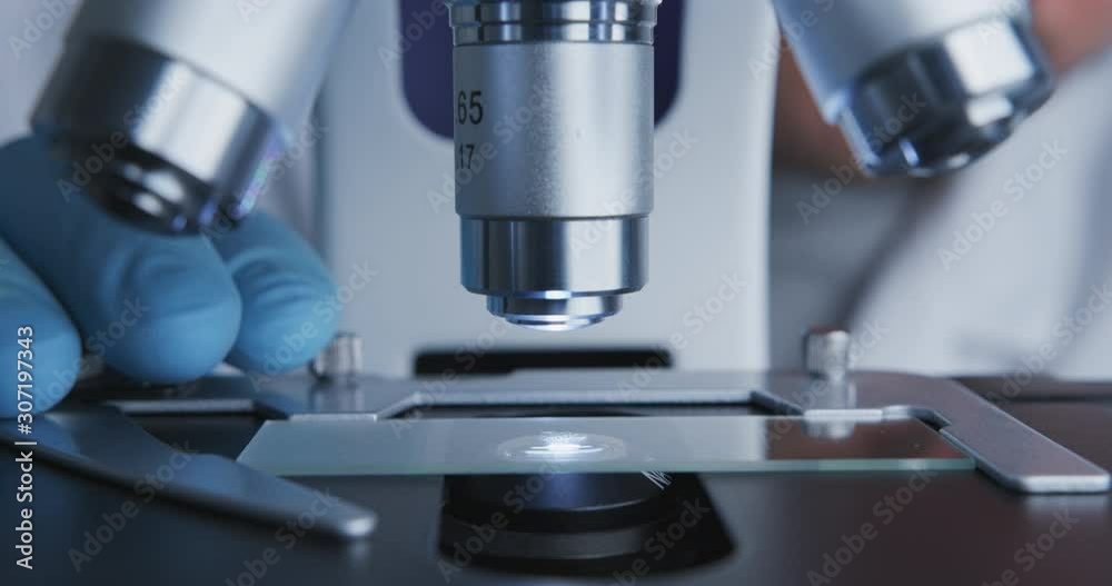 Close-up shot of sample slide and microscope with metal lens at laboratory.