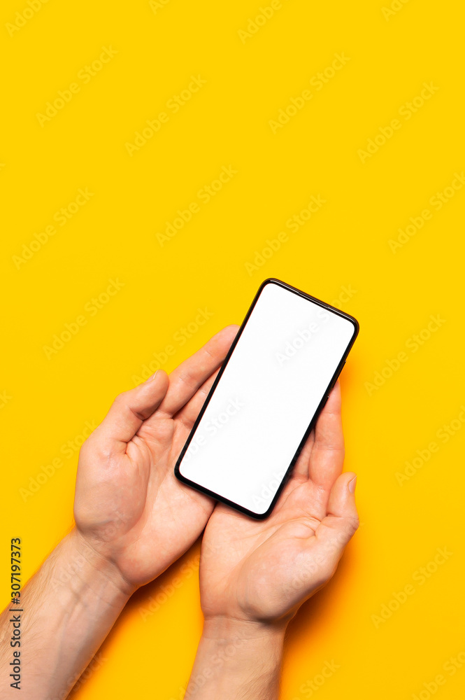 Male hands hold a modern black smartphone with white blank screen on yellow background. Modern technology, phone, gadget in hands, touch screen, template for your design. Mockup Male hands hold a modern black smartphone with white blank screen on yellow background. Modern technology, phone, gadget in hands, touch screen, template for your design. Mockup
