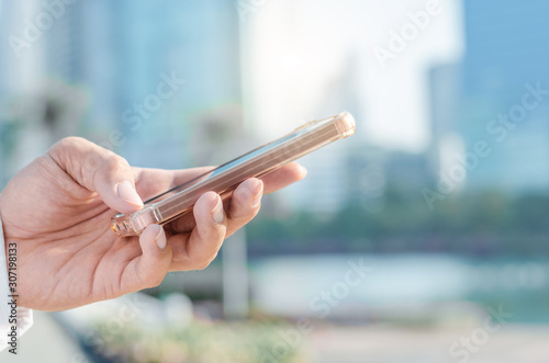 close up business man using hand typing smartphones and touch screen working search with app devices outdoor in city with sunrise and building background. 5G technology connecting the world.